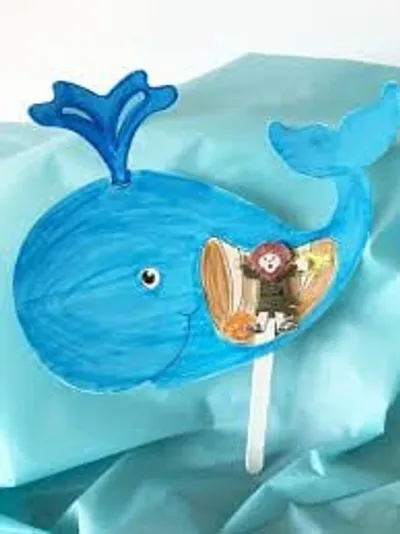 A child's illustrated blue whale craft with a felt figure of Jonah tucked inside